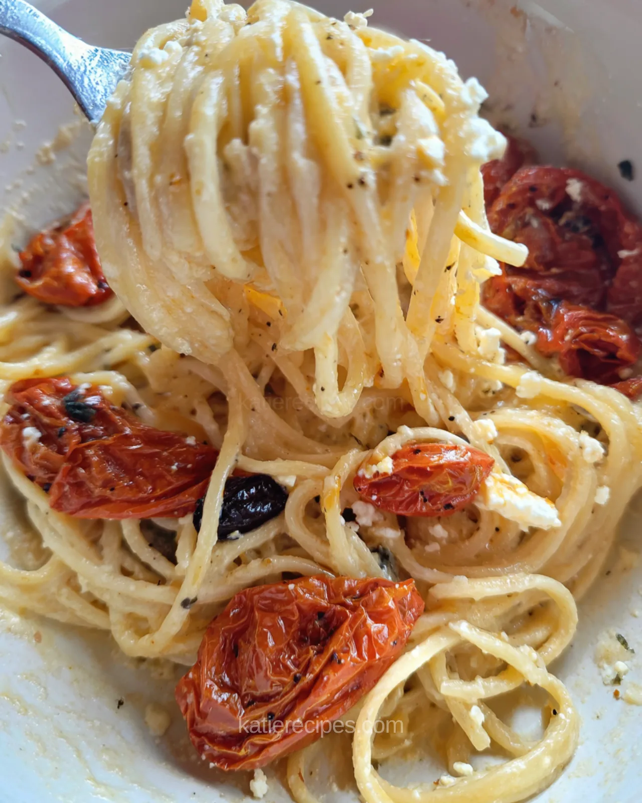 Forkful of creamy spaghetti with feta, roasted cherry tomatoes, and black pepper