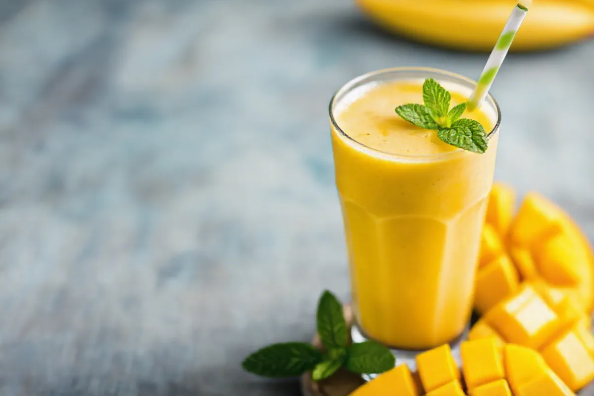 A vibrant glass of smoothie mit mango topped with fresh mint leaves.

