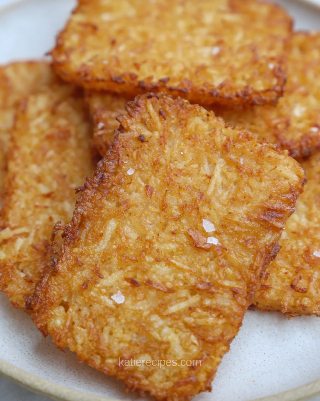 Crispy golden air fryer hash brown patties on a white plate with flaky salt