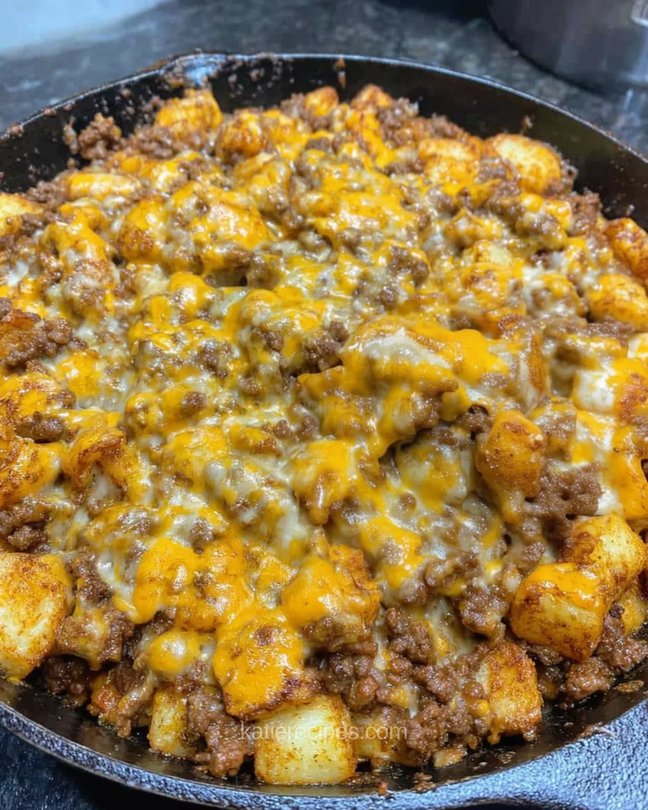 Sloppy joe potatoes topped with melted sharp cheddar in a cast iron skillet