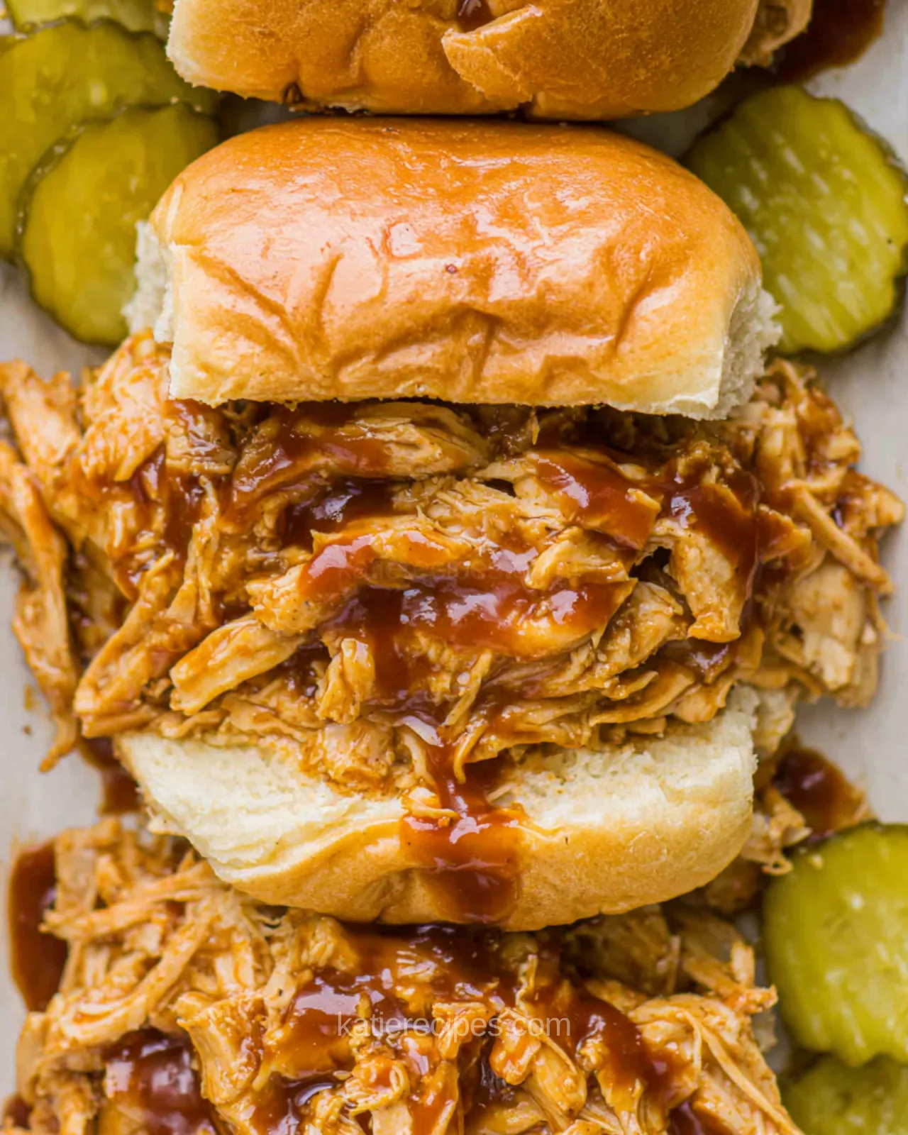 Close-up of pulled BBQ chicken sliders with sauce dripping down soft Hawaiian rolls