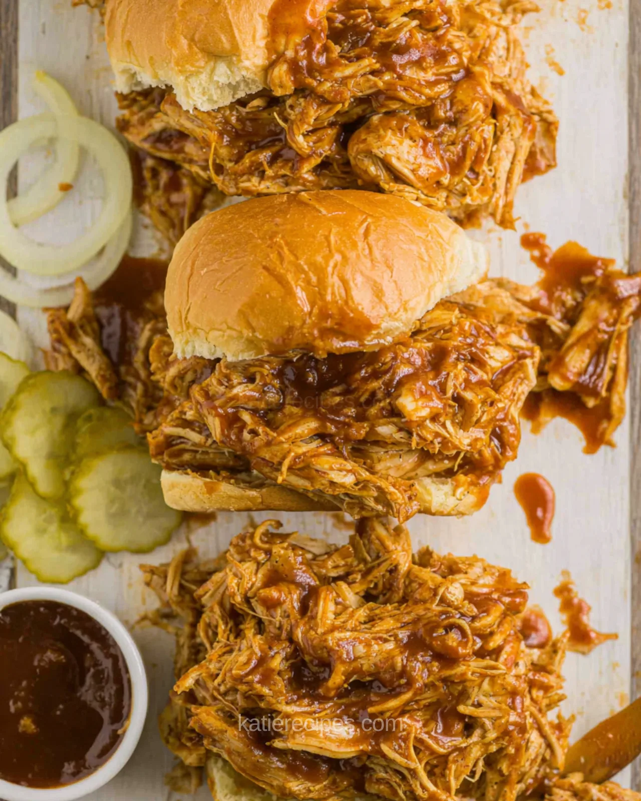 Crockpot BBQ chicken sliders on Hawaiian rolls with pickles, onion, and a dish of barbecue sauce