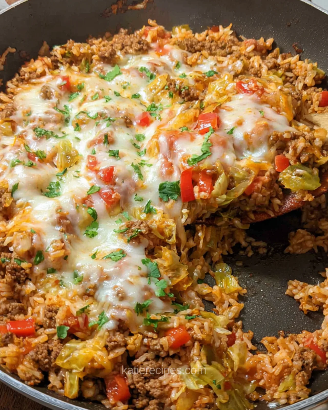 Cheesy cabbage roll skillet with a wooden spoon lifting a scoop of beef, rice, and cabbage