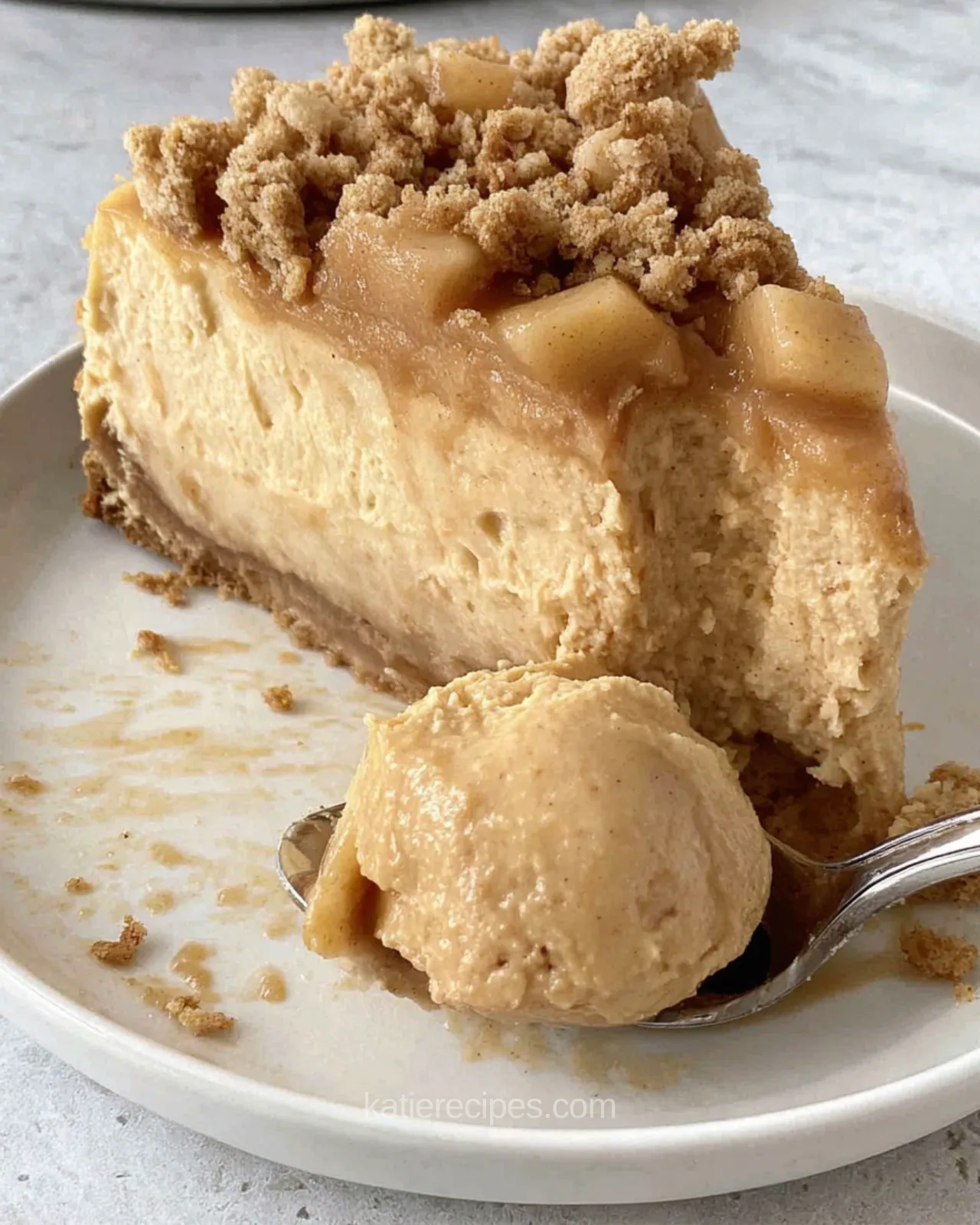 Slice of apple crumble pumpkin cheesecake showing golden filling, diced apples, and oat crumble