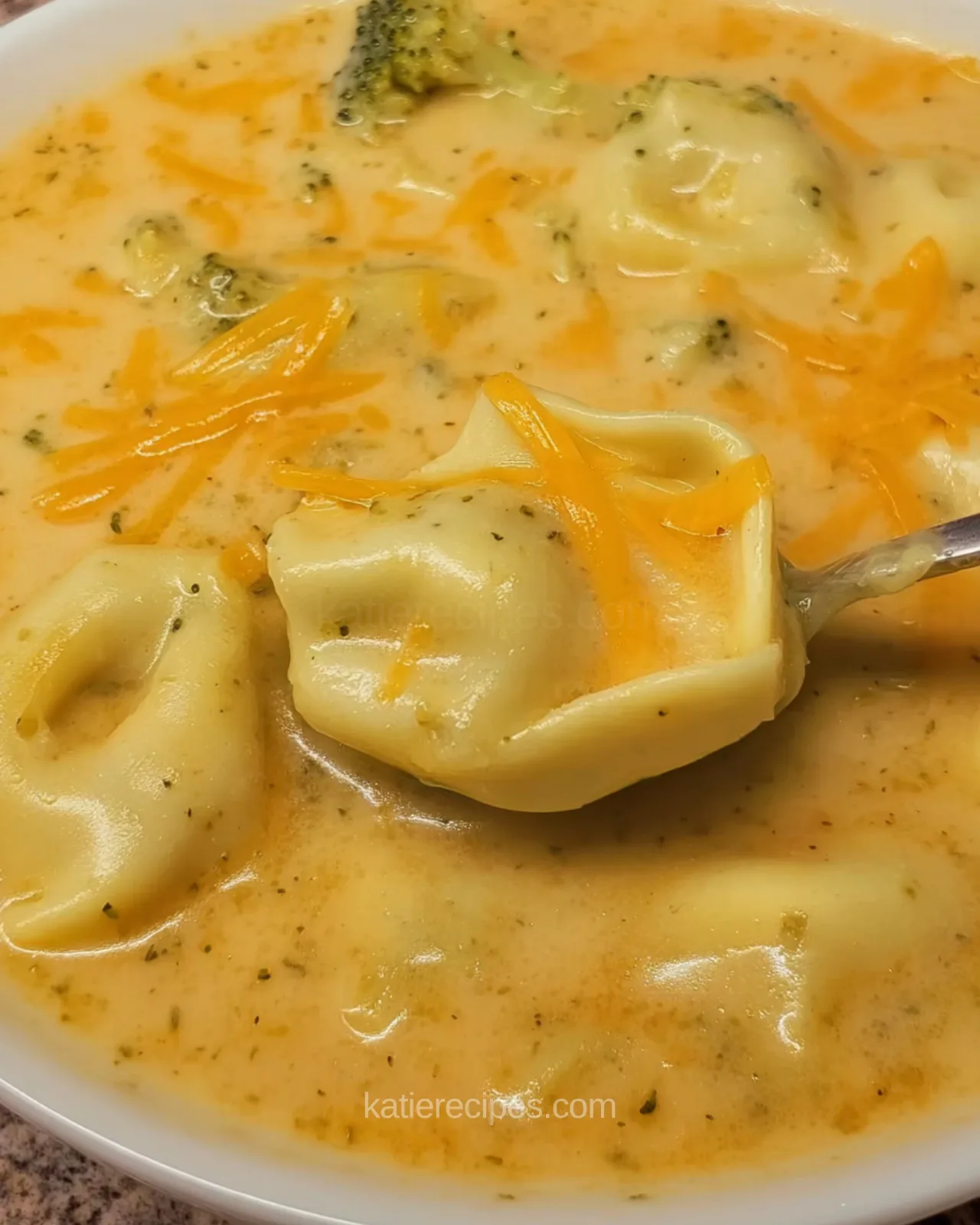 Spoonful of cheese tortellini lifted from creamy broccoli cheddar soup