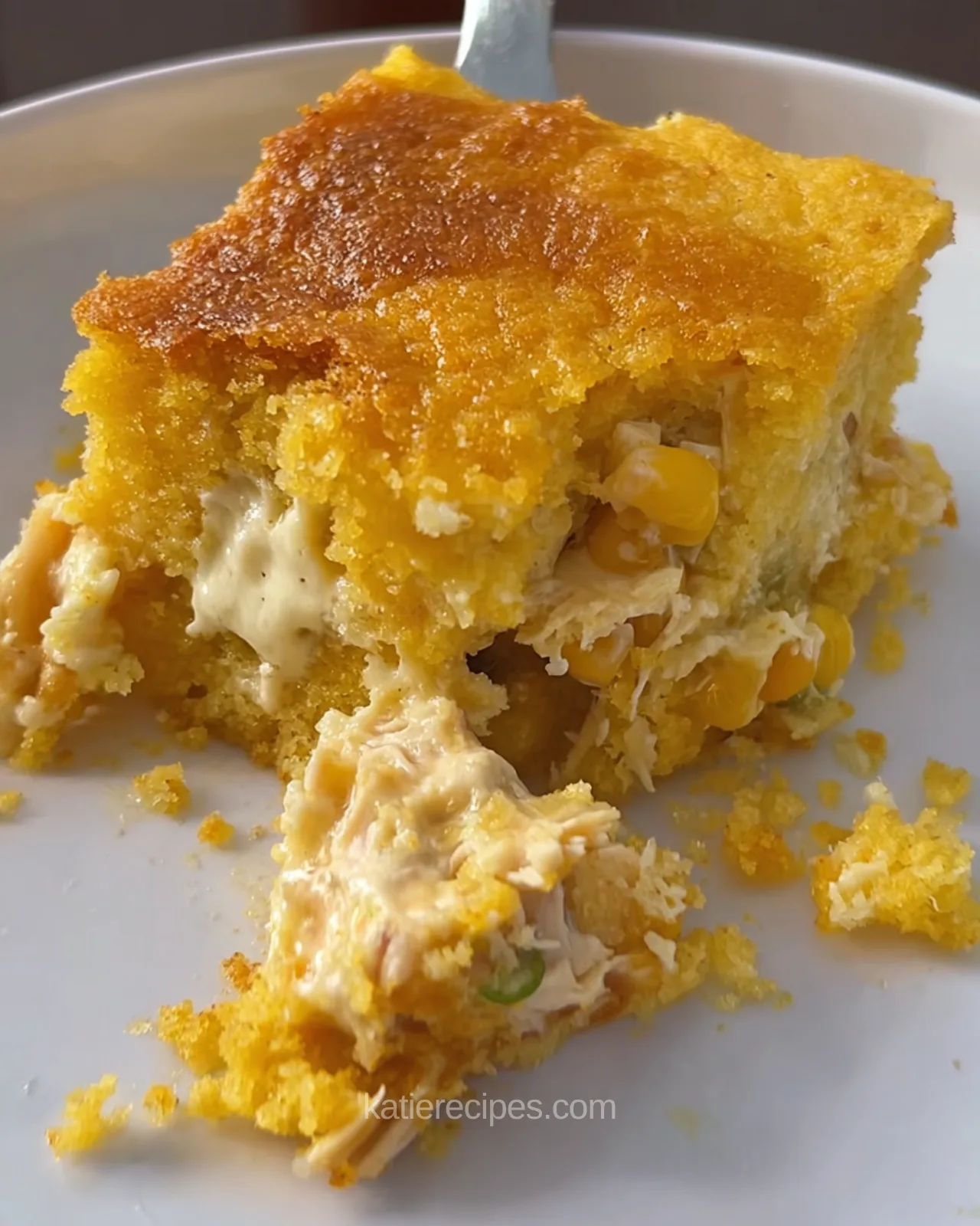 A square of chicken cornbread casserole served on a white plate with a forkful broken off showing creamy chicken filling and green onion