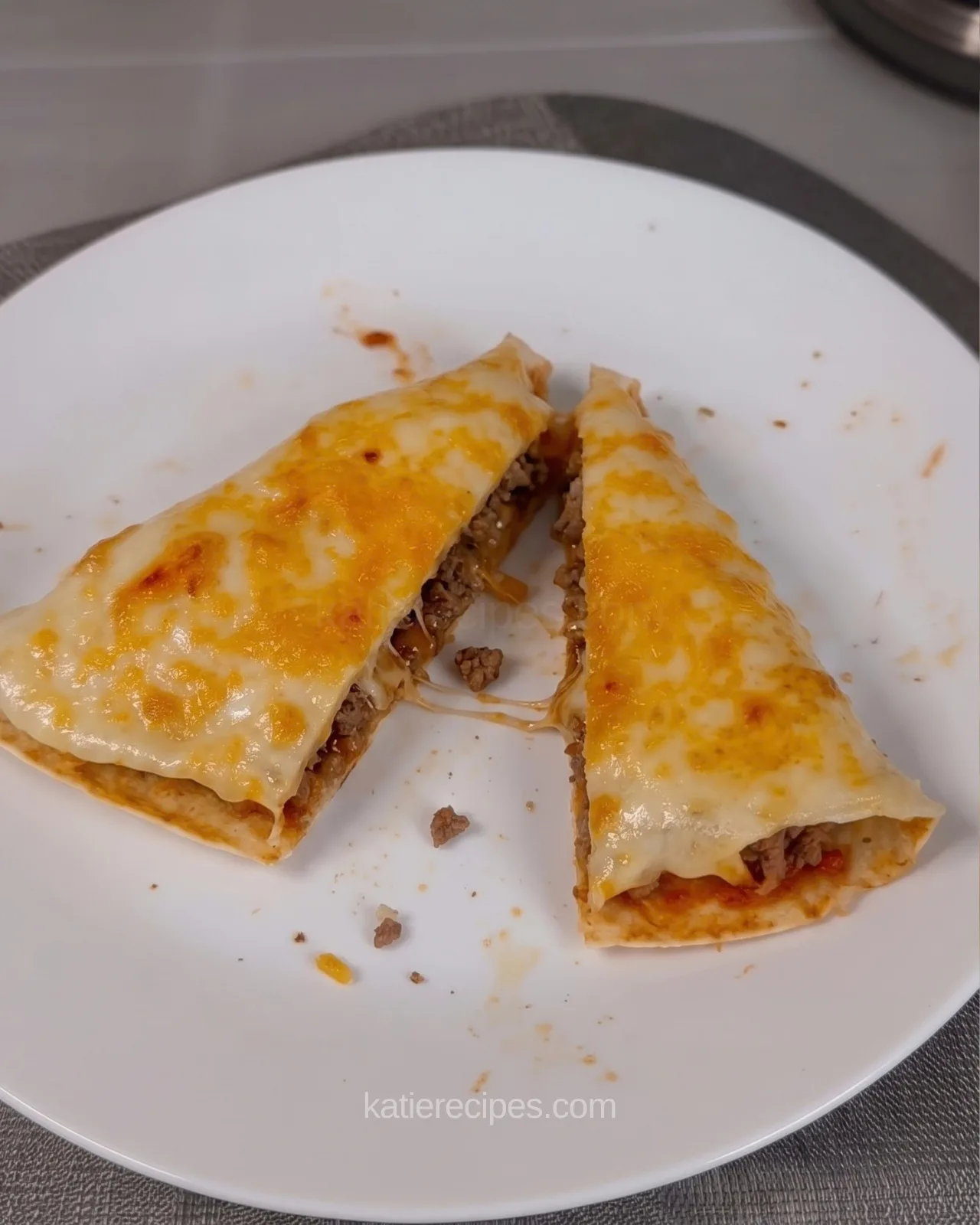 Beef and cheese tortilla triangle cut in half on a white plate, showing seasoned ground beef under melted golden cheese with a string of cheese between the halves