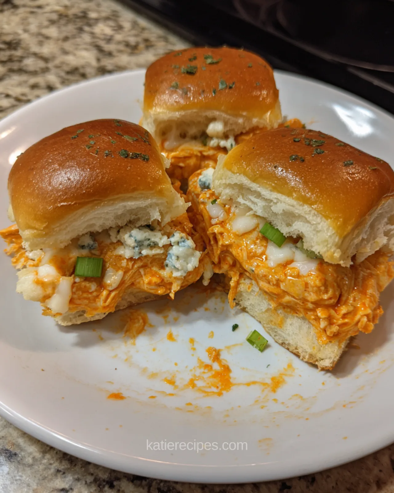 Buffalo chicken sliders cut open showing a thick filling of shredded chicken, melted cheese, blue cheese crumbles and green onion on a Hawaiian roll