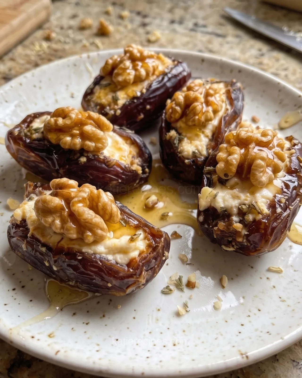 Five goat cheese stuffed Medjool dates topped with toasted walnut halves and honey on a white plate