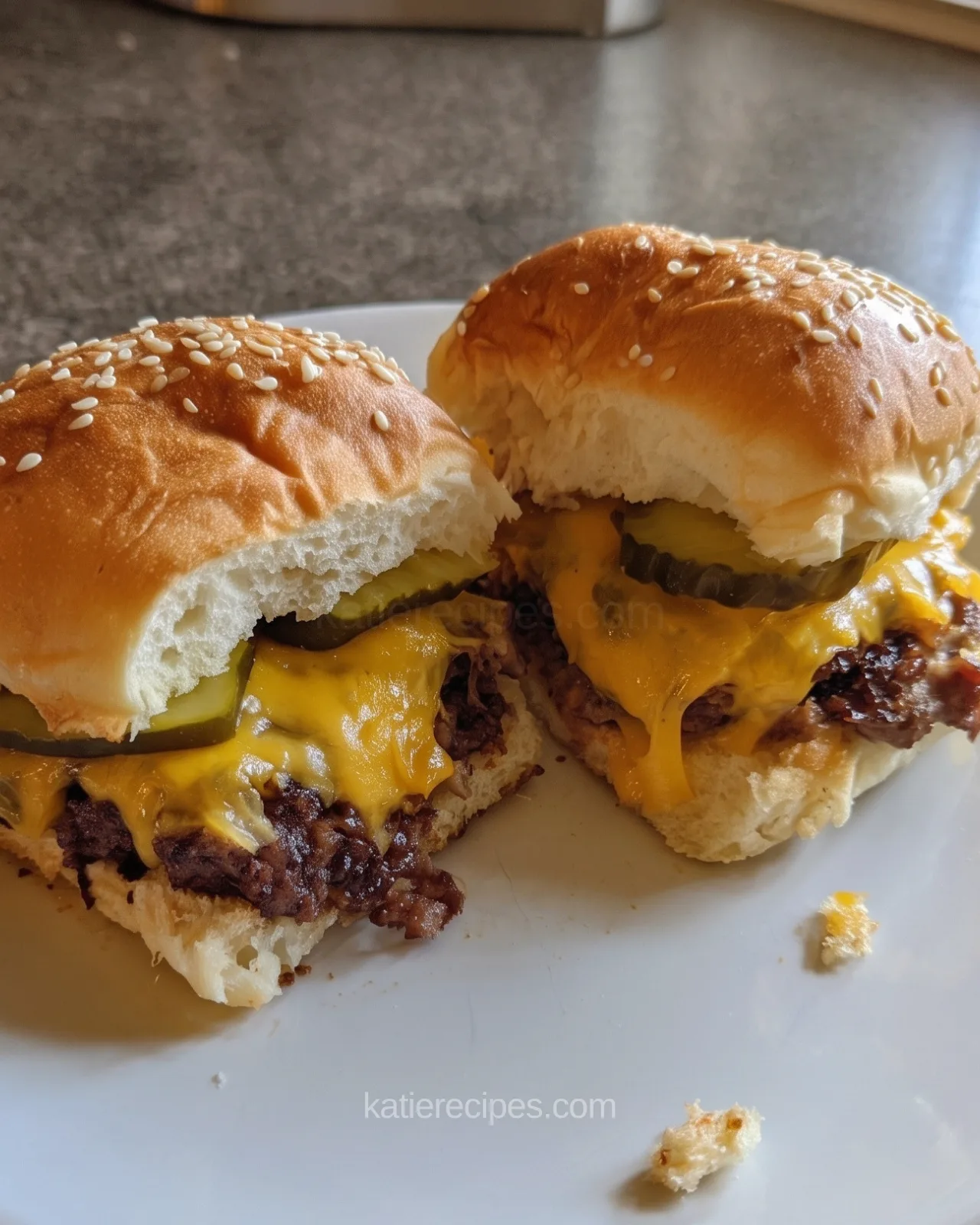 Two Hawaiian roll cheeseburger slider halves on a white plate with melted cheese, pickles and browned beef under sesame buns