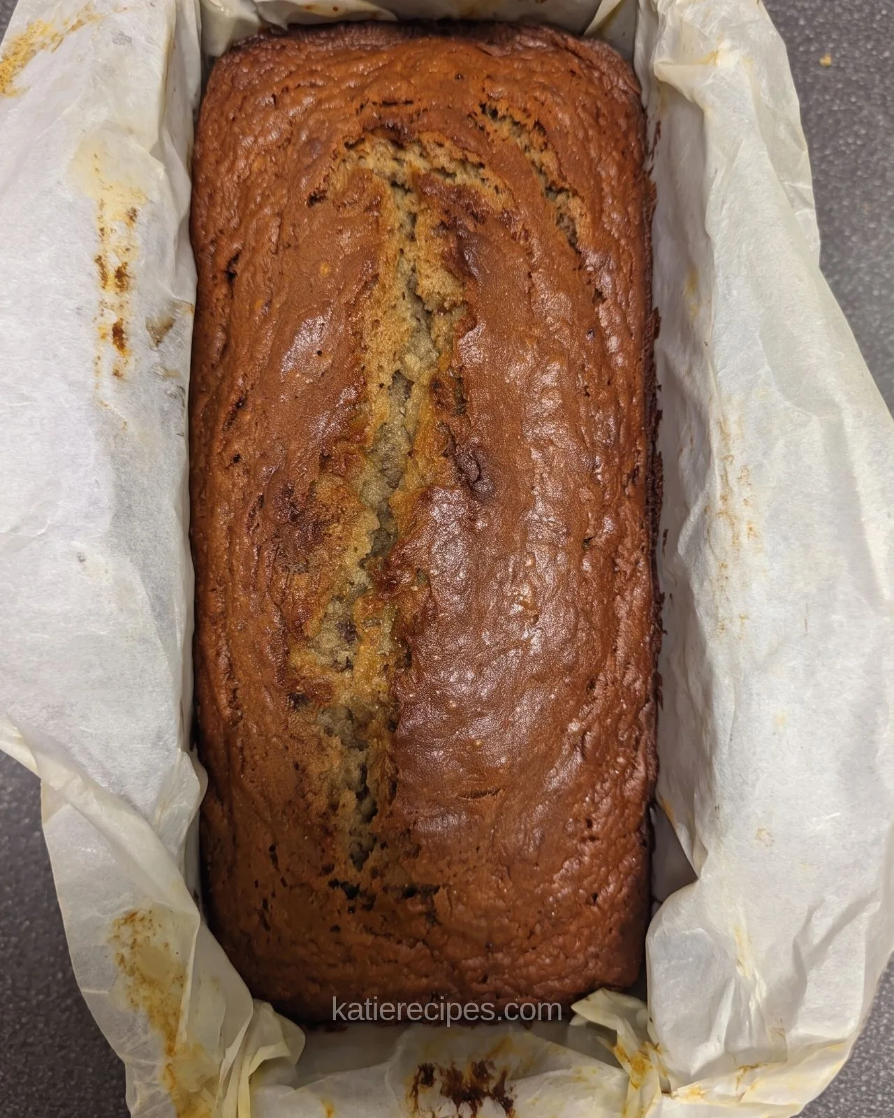 Top-down view of a baked protein banana bread loaf with a split down the center in a parchment-lined pan
