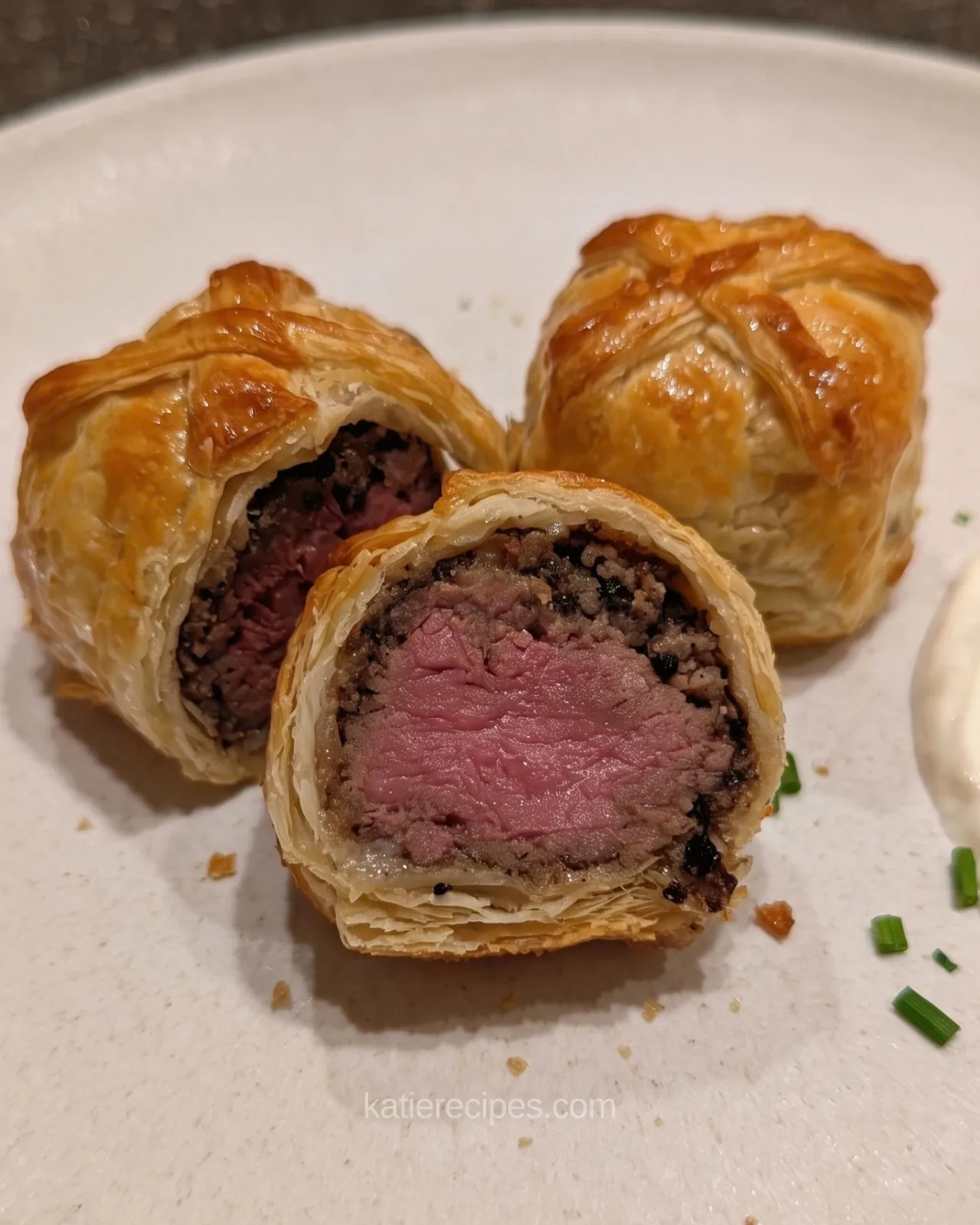 Mini beef wellington bite cut in half showing a medium-rare beef center surrounded by dark mushroom duxelles and flaky layered pastry