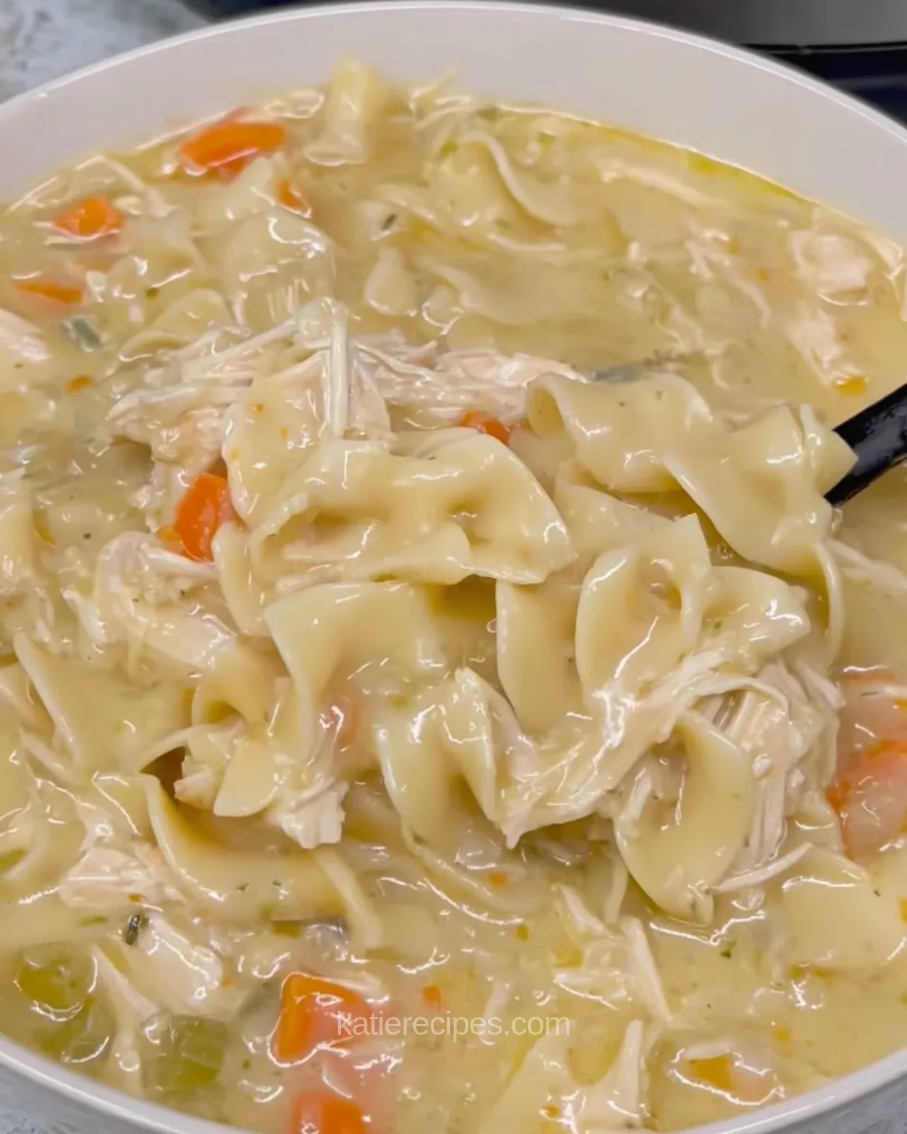 Bowl of creamy chicken noodle soup with wide egg noodles, shredded chicken and carrot pieces