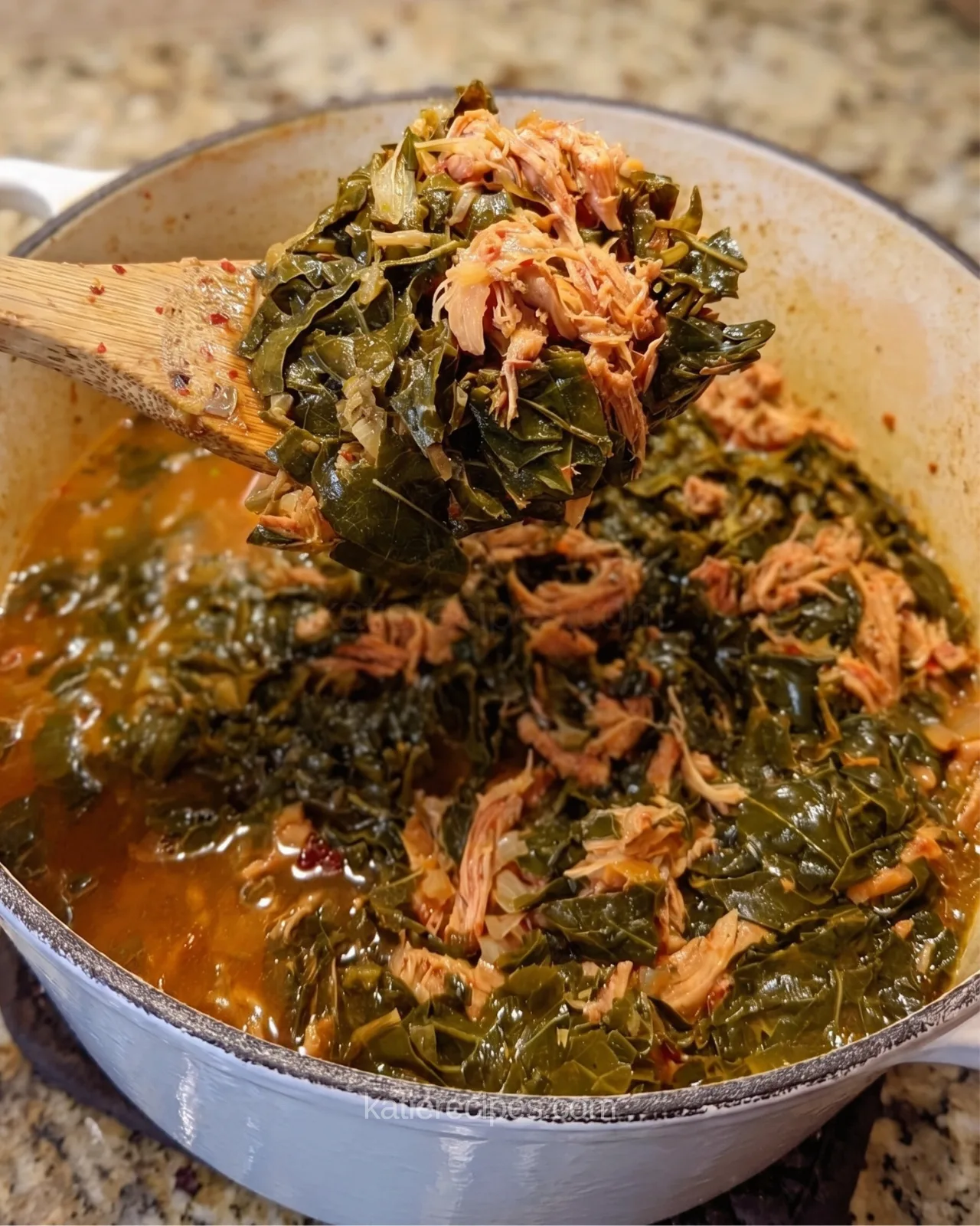 Wooden spoon lifting Southern collard greens with shredded smoked turkey out of a white pot of broth